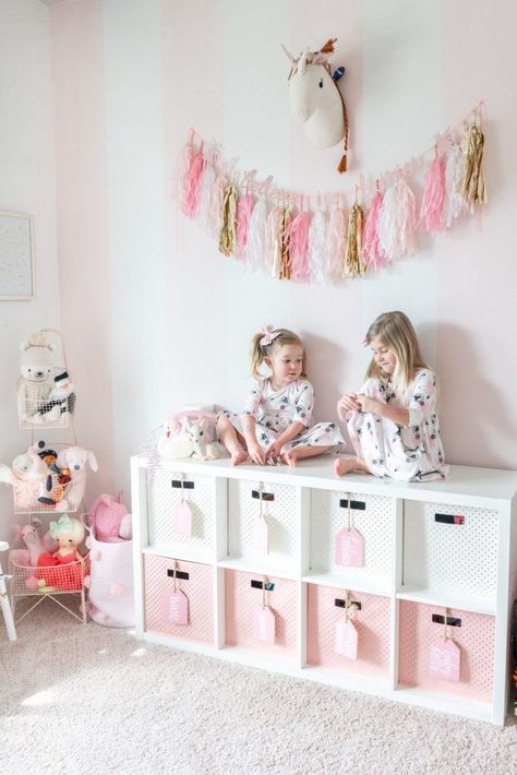 Sharing a full tour of our pink and white striped girls playroom with gold accents on the blog! We've lived in this playroom for almost 4 years now, and have updated quite a bit. We've added a few more storage and organizational pieces to make the room function well for us! #playroom #playroomdecor #pinkandwhitestripes #tassels #childrensdecor #kidsdecor #girlsroomdecor #unicorndecor #pinkandgold #goldaccents #homedecor Pink Dinosaur Room Decor, Girls Room Storage, Pink Playroom, Small Playroom, Kids Bedroom Storage, Shared Girls Room, Girls Playroom, Toddler Girl Room, Playroom Design