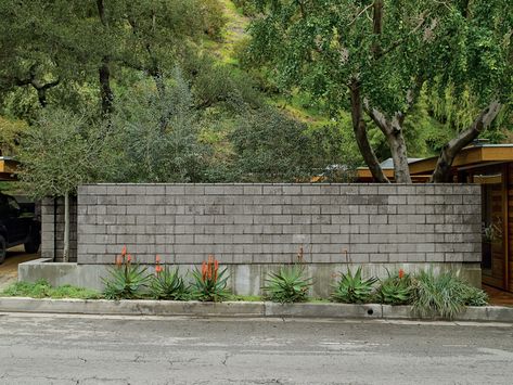 A wall of burnished concrete block protectively isolates their indoor and outdoor living areas from the busy road. Stem Wall, Busy Road, Cinder Block Walls, Modern Courtyard, Cinder Blocks, Modern Garage, Concrete Block, Mid Century Architecture, Cinder Block