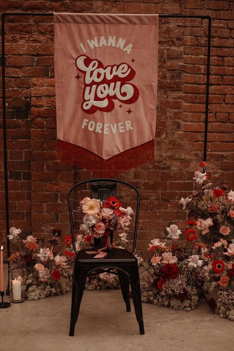 Dusty pink fabric wedding banner with red trimming and white and red retro writing on large black frame and floral decorations light pink roses, neutral and red poppies, echeverias, and baby's-breath Red Colour Scheme, Retro Writing, Wedding Streamers, Dusty Pink Fabric, Retro Wedding Theme, Unusual Wedding Venues, Light Pink Roses, Dusty Pink Weddings, Valentines Wedding