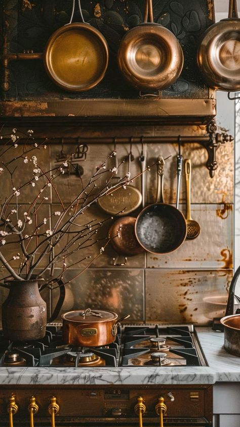 The photo depicts a rustic kitchen setup with a vintage aesthetic. In the foreground, there is a gas stove with brass and stainless steel detailing. Above the stove, several copper pots and pans hang from a brass rod mounted on a marble backsplash. To the left, there is a large earthenware vase with branches, adding a touch of natural decor. The overall ambiance combines luxury and antique charm. гиперреализм, профессиональное фото, HDR, 64k, освещение, гипердетализация, эстетично, красиво, 1200dpi, --ar 9:16. Oven Aesthetic Vintage, Copper Interior Design, Copper Fireplace, Copper Pots And Pans, Antique Kitchen Stoves, Steel Detailing, Beautiful Kitchenware, Earthenware Vase, Kitchen Setup