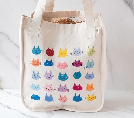 What's better than a cat? Many cats! This tote features an illustration of different cute cat faces and expressions in a variety of bright colors. Perfect for any cat lover! Made from 100% certified organic cotton in a medium heavy weight (9 oz/yd² (305 g/m. Featuring a small Econscious tag on handle base and a larger materials tag on the interior. A gusseted side means tons of room and the volume is similar to a grocery bag.  * 100% Certified Organic Cotton: Made from ring-spun cotton that makes a very strong fabric. This cotton is grown without the use of pesticides, herbicides, or other chemical fertilizers. * Cotton web handles: These handles, with reinforced stitching, make the bag comfortable to carry.  * Spacious interior: It has one large open main compartment to fit all you need. Cat Tote Bag Design, Colorful Cat Art, Tote Bad, Cat Tote Bag, Cute Cat Face, Cat Faces, Colorful Cat, Painted Tote, Cats Tote Bag