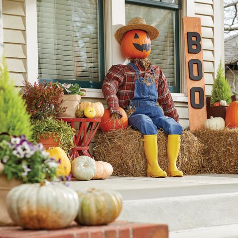 A homemade scarecrow sits on a front porch. Front Porch Scarecrow Ideas, Scarecrow Fall Decor Outside, Diy Sitting Scarecrow For Porch, Porch Scarecrow Diy, Scarecrow Porch Decor, Diy Sitting Scarecrow, Scarecrow Decorations Front Yards, Sitting Scarecrow Diy, How To Make A Scarecrow Diy