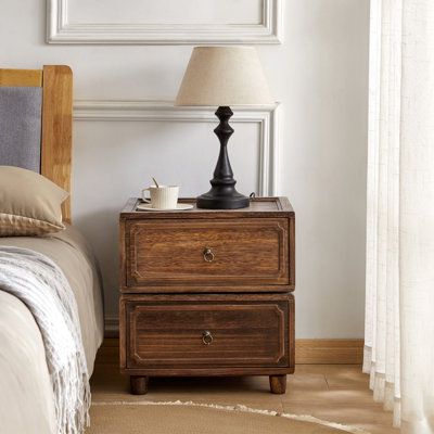 This nightstand brings a touch of farmhouse charm and transitional style to your bedroom. Crafted from kiln-dried solid paulownia wood, it features a stacked, rectangular shape with a finished back, ensuring it looks great from every angle. The two drawers glide smoothly on roller glides, offering easy access to your bedside essentials. Antique bronze ring handles add a vintage touch, complementing the rustic appeal of the paneled drawer fronts. With its versatile design, this nightstand can als Metal And Glass Nightstand, Dark Wooden Nightstand, Dresser As Bedside Table, Chunky Nightstand, Bedroom Night Stand Decor, Cozy Masculine Bedroom, Cape Interior, Bedroom Transitional Style, Traditional Bedroom Furniture Sets