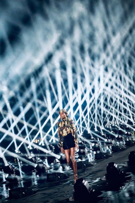 The Eiffel Tower turned gold, and light beams illuminated the sky above Paris for Saint Laurent’s dramatic SS20 show.   Bureau Betak designed the outside stage for Anthony Vaccarello’s show, taking things back to basics. Models walked down a runway lined with over 100 powerful spotlights, with pillars of white light directed upwards towards the heaven in a light show reminiscent of a rock show.   Photography by Richard Gianorio Outside Stage, Ysl 2024, Fashion Show Lighting, Catwalk Runway Stage Set Design, Stage Lighting Design Dance, Led Stage Design Events, Eiffel Tower Fashion, Runway Lights, Runway Lights Airport