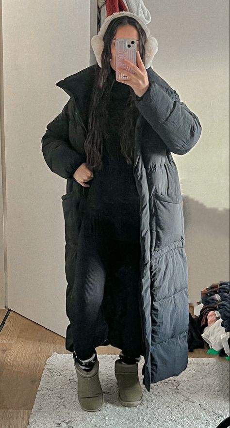 a mirror photo of a girl with mermaid wavy hair. She is wearing a black high neck jumper paired with black seamless leggings. to add an extra layer or warmth she is also wearing black fluffy socks with khaki ugg ultra minis and a long puffer padded black coat. to keep her even warmer she is wearing brown ear muffs Maxi Puffer Coat Outfit, Ear Muff Outfit, Padded Coat Outfit, Styling Black Leggings, Ear Muffs Outfit, Boots Black Outfit, Mini Ugg Outfit, Puffer Jacket Aesthetic, Earmuffs Outfit