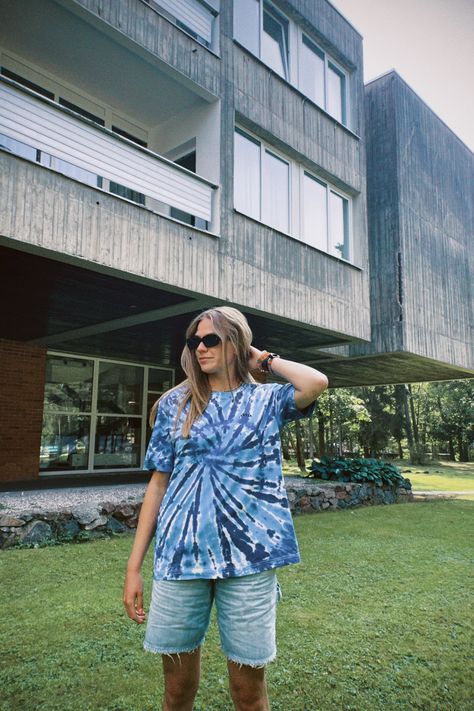 Blue tie dye t-shirt on a model standing in front of a building, on the grass. Tie dye shirt is with spiral pattern of blue shades baby blue and cobalt. Model is wearing oversize relaxed fit streetstyle tee with short sleeves and small listee logo on the front and oversized jean shorts. Outfit Ideas For Summer 2023, Outfit Ideas For Summer, Tie Dye Tshirt, Tie Dye Fashion, Tie Dye Outfits, Unique Ties, One Colour, Festival Looks, Tie Dye Patterns