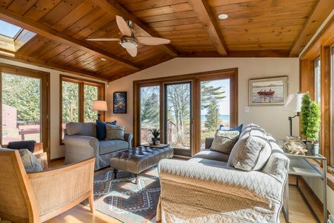 Several windows, glass doors and a skylight fill this lake house sunroom with ample natural light. The wood paneled ceiling works perfect  with the natural surroundings and complements the door frames and windows. Cozy seating makes the space even more inviting. Wood Paneled Ceiling, Wood Ceiling Panels, Paneled Ceiling, Decorative Ceiling Tile, Cozy Seats, Beautiful Cabins, Wood Ceiling, Cozy Seating, Tiles Design