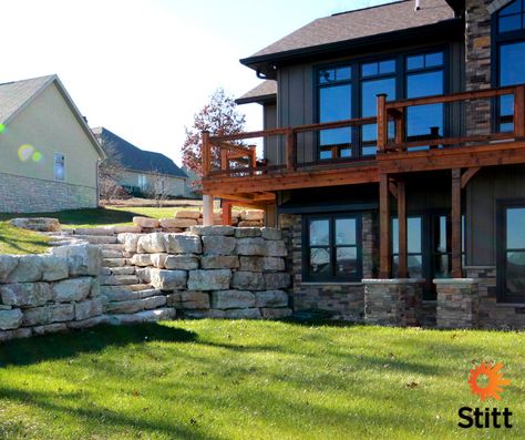 If you plan to build a home in the #Ozarks, chances are you’ll encounter both hills and rocks and lots of them!   A sloping site is perfect for a walk-out basement, providing your home with separate yet connected living areas. Design a retaining wall and outdoor stairs to the lower level using large slabs of native rock. Source natural materials locally, and they'll look and perform beautifully for years to come!  #stitthomes #landscapedesign Back Deck Over Walkout Basement, Walkout Basement Patio Retaining Wall, Walkout Basement Retaining Wall Ideas, Retaining Wall Walkout Basement, Walkout Basement With Retaining Wall, Walkout Basement Pool, Walk Out Basement Retaining Wall Ideas, Basement Retaining Wall Ideas, Walkout Basement Retaining Wall