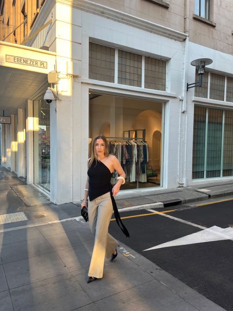 Asymmetrical one shoulder black top with y2k low rise boot leg tan pants, pointed toe kitten mules, Jimmy Choo clutch, and bangles. Golden hour lighting, outfit inspo, street style, style inspo One Shoulder Black Top, Golden Hour Lighting, Outfit Inspo Street Style, Jimmy Choo Clutch, Tan Legs, Tan Pants, Black Top, Golden Hour, Content Creator