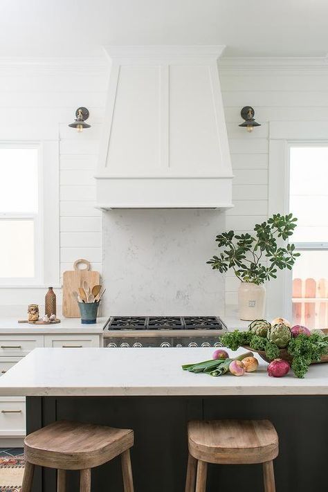 Barn sconces fixed to a white shiplap backsplash flank a white wood hood mounted above a stainless steel range placed between by white shaker drawers adorned with nickel hardware and a white quartz countertop. Kitchen Vent Hood, Stove Backsplash, Kitchen Vent, Shiplap Backsplash, Farmhouse Backsplash, Kitchen Styles, Best Farmhouse, Victorian Kitchen, Diy Backsplash