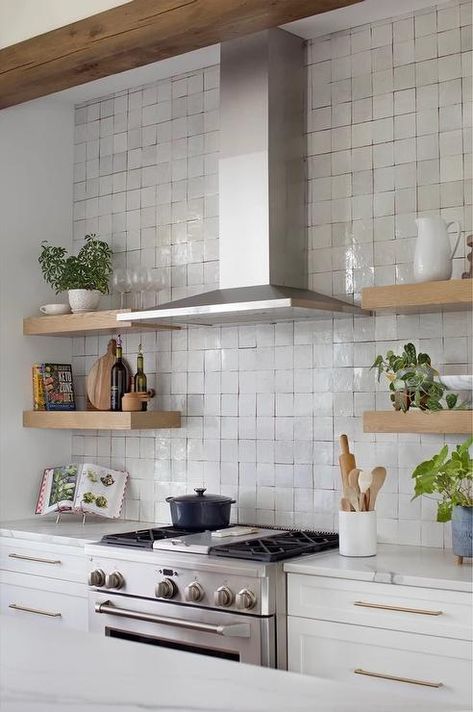 A stainless steel range hood is mounted to gray glazed backsplash over a stainless steel oven range and between stacked oak floating shelves. Tile Behind Range Hood Open Shelves, Open Shelf Upper Cabinets, Floating Shelves By Range Hood, Hood Range With Open Shelves, Range Hood Shelving, Oven Hood With Open Shelving, Stove With Floating Shelves, Kitchen Shelves Around Hood, Extractor Hood Ideas Open Shelves