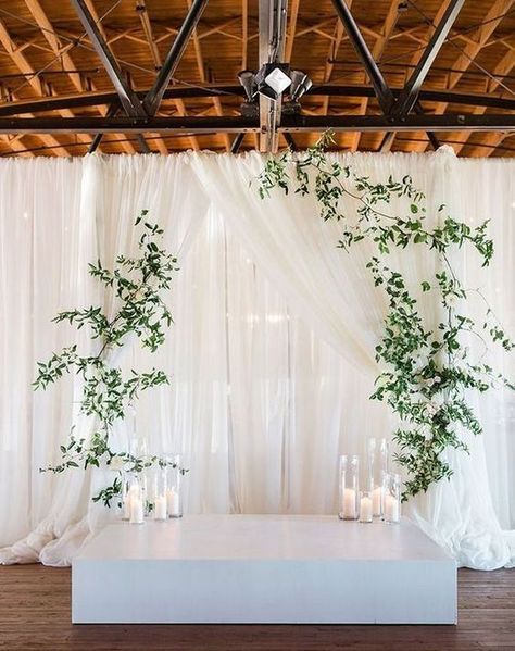 a minimalist wedding altar a white platform, candles, greenery hanging on curtains Wedding Ceremony Wall Backdrop, Modern Ceremony Backdrop, Wedding Ceremony Backdrops, Candles Reception, Modern Greenery, Draping Wedding, Wedding Ceremony Ideas, Simple Elegant Wedding, Wedding Ceremony Backdrop