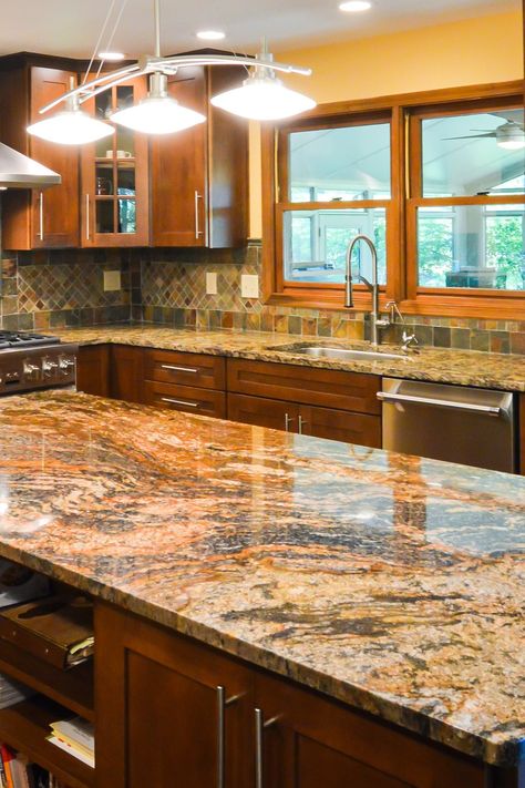 Warm dark wood cabinetry contrasts the cream travertine flooring in this large, open-plan outside grill area. Also, Magma Gold tops made a good color matching. #magmagoldgranitekitchencountertop #magmagoldgranitekitchencounter #magmagoldgranitekitchentop #goldgranitecolors #goldencolorgranitecountertop #darkwoodcabinet #darkcolorcabinetry #darkcupboard #multicolorbacksplashtile #slatelookbacksplashtile #darkshakercabinet #pendantlight #darkcabinetmagmagoldgranitecounter #darkcabinetrygoldencolor Black And Gold Granite Countertops Kitchen, Dark Brown Marble Countertops Kitchen, Orange Granite Countertops Kitchen, Atlas Granite Countertop, Kitchen Backsplash With Brown Granite, Granet Countertop Kitchen, Orange Granite Countertops, Granite Countertops With Brown Cabinets, Brown Granite Countertops Kitchen