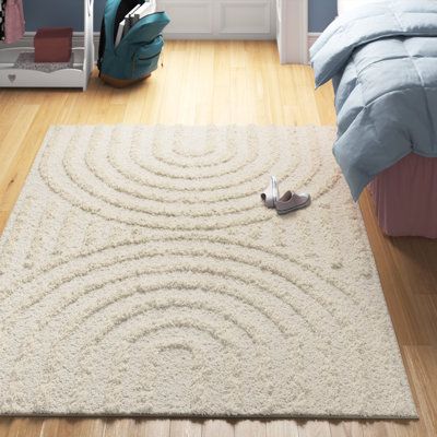 Minimalism meets fluid style in this neutral area rug. Enlivening your office or bedroom with a contemporary vibe, it shows off a high-low pile with raised curved lines that form two mirrored rainbow-inspired shapes in a light beige hue. Power-loomed from polyester, it features a generous 1.18'' pile height that provides plush underfoot cushioning in rooms that see light foot traffic. Plus, it's stain-resistant, so it holds up in busy homes. Although it has a backing, we recommend pairing it wit Neutral Area Rugs, Cream Area Rug, Shag Area Rug, Ivory Rug, White Area Rug, Beige Rug, Beige Area Rugs, Geometric Rug, Decoration Design