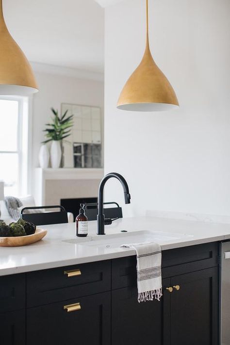 Gold lights illuminate a black shaker kitchen peninsula accented with brass hardware and a white quartz countertop finished with a sink and an oil rubbed bronze gooseneck faucet. Black Shaker Kitchen, Gold Lights, Replacing Kitchen Countertops, Kitchen Peninsula, Best Kitchen Design, Black Faucet, Black Kitchen Faucets, Brown Kitchens, Home Luxury