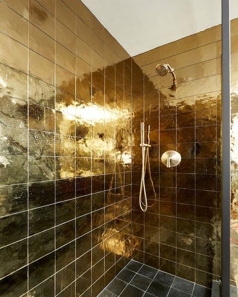 A brushed gold shower head is mounted to shiny gold grid shower wall tiles over black grid floor tiles. Gold Tiles Bathroom, Amber Interiors Bathroom, Gold Shower Head, Golden Bathroom, Gold Tiles, Gold Floor, Shower Wall Tile, Gold Tile, Gold Mosaic