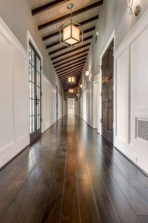 Gorgeous hallway features a sloped ceiling dotted with dark stained wood beams and caged Lanterns with Paper Shades. Stained Wood Beams, Houses Inside, Hallway Ceiling, Luxury Farmhouse, Long Hall, Pole House, Hall Lighting, Slanted Ceiling, Dark Wood Stain