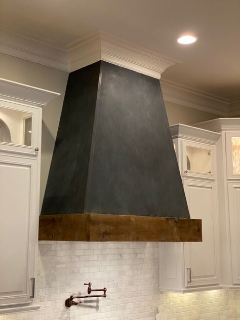 We used Zinc sheet metal to cover this vent hood and added a black hand applied patina. The wood band is 200 year old reclaimed wood from a home in Jefferson, Ga. #vent #zinc #patina #reclaimed #reclaimedwoodfurniture #kitchen #kitchendecor #kitchendesign #kitchendesignideas #aesthetic Black Metal Hood Kitchen, Metal Hoods Over Stoves, Black Range Hood With Wood Trim, Black Hood Cover Kitchen, Black And Wood Range Hood, Metal Range Hood Ideas, Metal Stove Hood, Black Stove Hood, Black Vent Hood