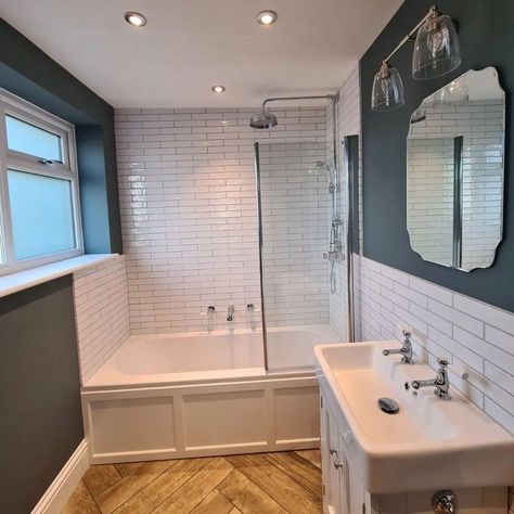 Bathroom. Bath along end wall with shower screen. Half tiled with metro tiles. Basin on right wall set in a vanity. Silver vintage  style mirror above. Window on left wall which is painted a navy blue. Herringbone wood style flooring. White Metro Tiles Bathroom, White Metro Tiles, Metro Tiles Bathroom, Blue And White Bathroom, Bungalow Bathroom, Pretty Bathroom, Built In Bath, Loft Bathroom, White Bathroom Tiles