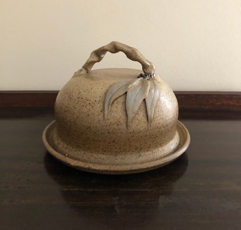 Earthy, rustic and beautifully handmade stoneware pottery butter dish in shades of brown and beige, and decorated with applied gum leaves and nuts on the both the lid and base plate.  Sometimes referred to as a European Butter Dish, the lid is in the shape of a dome. The base plate is flat and round, with a slight lip to ensure your cheese or butter doesn't slip away.  Measuring 19cm in diameter from edge to edge, it is idea for a small butter block or brie wheel.   The dome lid has a crimped ha Round Butter Dish, Brie Wheel, Butter Block, European Butter, Pottery Butter Dish, Gum Leaves, Australian Vintage, Handcrafted Pottery, Brie Cheese