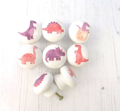 Purple and Pink cute dinosaur door knobs. Handmade kids drawer pulls with fun girl's dinosaur designs on. These gorgeous  dino door handles are a beautiful touch to a dinosaur bedroom, play room or nursery.  These drawer knobs are quick and easy to fit at home and you can choose each individual design from the drop down variations and add them individually to your basket.  **PRICE IS PER KNOB**  Each wooden knob is hand painted with white chalk paint and then decorated with a gorgeous variety of Dinosaur Bedroom Girl, Pink Dinosaur Room, Handles Ceramics, Toddler Dinosaur Room, Dino Bedroom, Kids Drawer, Whimsical Nursery Decor, Dinosaur Kids Room, Dino Nursery