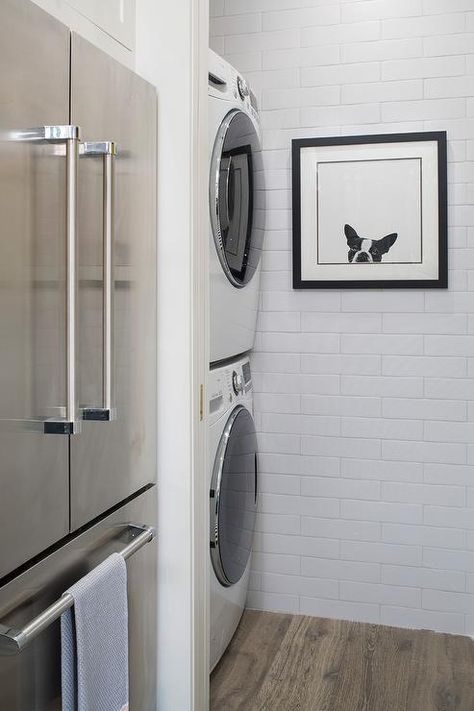 A stainless steel refrigerator with a freezer drawer is inset beside a linear white tiled nook fitted with a stacked white front loading washer and dryer and finished with a dog photography art piece. Stacked Laundry Room Ideas, Stacked Laundry, Honeymoon House, Stacked Laundry Room, Laundry Room Storage Shelves, Small Laundry Room Organization, Taupe Walls, Stylish Laundry Room, Stackable Washer And Dryer