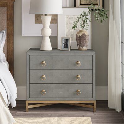 This nightstand provides you with tons of room to store your bedtime necessities and add plenty of glam style to your bedroom. It's crafted from engineered wood with a neutral stone-like coating that works with a variety of color schemes. The upper compartment rests on a sleek gold-finished metal frame with matching crossbar supports and ring pulls on each of the three drawers. The drawers give you a spot to keep linens and other essentials organized and in one place. Measuring 35" wide, this be Brushed Gold Ring, Gold Nightstand, Gray Nightstand, Nightstand Wood, Metal Nightstand, Ring Pulls, Style Nightstand, 3 Drawer Nightstand, Gold Bedroom