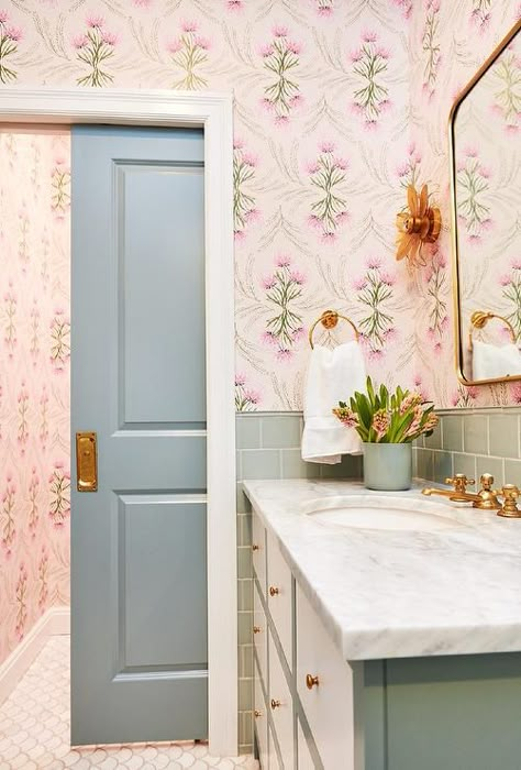 A green pocket door opens to a chic pink and green contemporary girls bathroom boasting white fan floor tiles and a cream and green apothecary-style washstand adorned with brass knobs and a honed marble countertop. Green Bath Vanity, Styled Bathroom, Cottage Traditional, Pink And Green Wallpaper, Green Backsplash, White Fan, Honed Marble, Cottage Bathroom, Backsplash Tiles