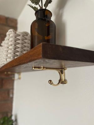 A classic solid brass shelf bracket complete with a hook at the bottom, perfect for hanging other items from like tea towels in the kitchen or items in a bathroom. All of our brass finishes are unlacquered to age further naturally over time. To pr... Brass Shelf Brackets Kitchen, Shelf With Brass Brackets, Classic Wall Shelf, Brass Railing Shelf, Hanging Shelves Bathroom, Shelf Bracket Ideas, Ensuite Makeover, Vintage Hooks Wall, Hearth Design