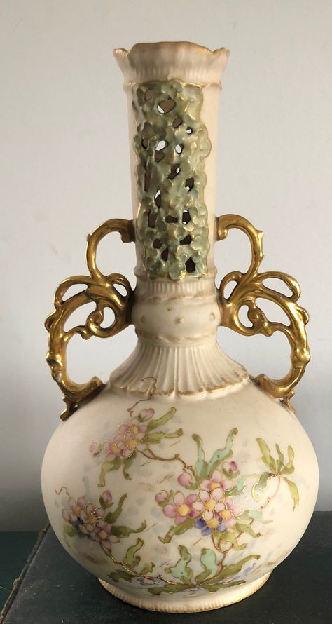 Antique vase by Wien Teplitz, made in Austria. Approximately 8 inches in height. It has a cream background with gilded handles and hand painted flowers in soft pink and green with gold accents. The top portion of the vase is pierced. The back stamp for the company (pictured) dates it to the early 20th century.  Please note there is some wear to the gilding on the handles and a small nick along the bottom rim. This vase has been used (please see the photo showing the inside.) Lovely and delicate. Fantasy Vase, Antique Vases Vintage, Vases Antiques, Vintage Vessel, Green With Gold Accents, Victorian Vases, Amphora Vase, Vases Ceramic, Antique Vases