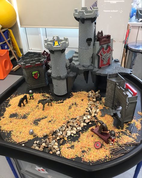 The tuff tray has a large grey play mobile castle at its centre .It’s surrounded by dry coloured rice and a small pebble pathway leading to the castle .There are a couple of play mobile horses and figures. Castle Sensory Bin, Eyfs Castles, Castles Eyfs, Fairytales Eyfs, Medieval Sensory Bin, Fairytale Tuff Tray, Castle Role Play Area, Castle Continuous Provision, Knights And Castles Topic