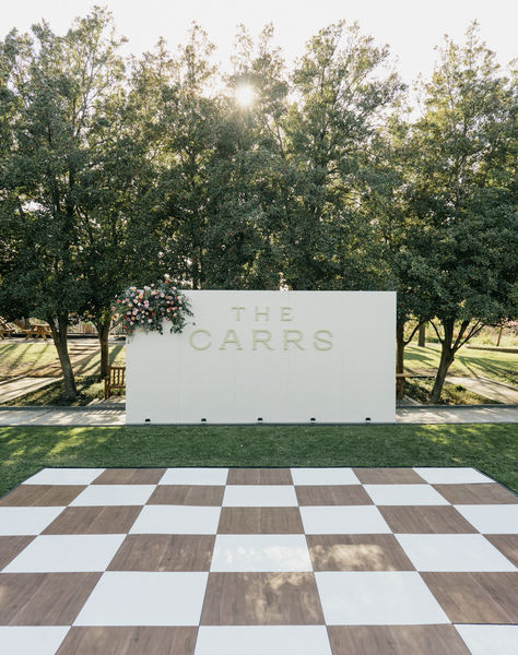 Wooden and white checkered dance floor with stunning custom wall! Perfect for welcoming guests to dance!! Stunning and unique flooring for Dallas wedding!  #socialllamaevents #dallaswedding #dancefloor #customdancefloor #weddingrentals #weddingdeocr #weddinginspo #weddingfloor #customrentals #dallasrentals #customwedding #socialllama #customrentals #weddinginspiration Checkers Dance Floor, Wedding Decor Dance Floor, Outdoor Reception Dance Floor, Wedding Dance Floor Alternatives, Checkered Dance Floor Outdoor Wedding, Brown And White Checkered Dance Floor, Homemade Dance Floor Wedding, Brown And White Dance Floor, Diy Checkered Dance Floor