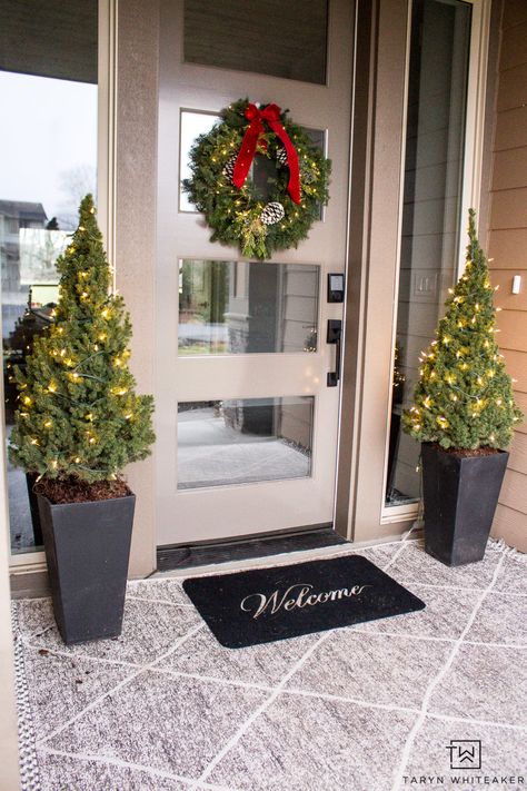 Keep it simple with this Classic Christmas Porch. Featuring layered porch rugs, mini Christmas trees and a fresh green wreath with red bow! Christmas Front Porch Trees, Christmas Tree Planters Front Door, Front Door Christmas Trees In Pots, Entry Door Christmas Decor, Christmas Decor Ideas Porch, Christmas Decor Front Door, Small Front Porch Christmas Decor, Porch Rugs, Christmas Entrance