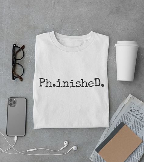 "Ph.inisheD. Soft Cotton Unisex T-Shirt | Graduation Gift | Gift T-Shirt | Doctor T-Shirt | Funny T-Shirt | PhD T-Shirt | Dr. T-Shirt The unisex soft-style t-shirt puts a new spin on casual comfort. Made from very soft materials, this tee is 100% cotton for solid colors. Heather colors and sports grey include polyester. The shoulders have twill tape for improved durability. There are no side seams. The collar is made with ribbed knitting to prevent curling damage.  Designed by Win's Market and s Etsy Pod, Phd Shirt, Pizza Graphic, White Tshirt Men, Phd Student, Grad School, Grad Gifts, 2024 Vision, School Shirts