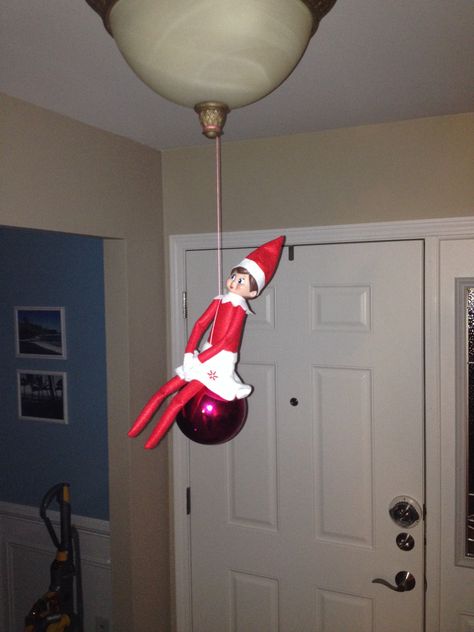 Elf on the shelf Day 8.  Jingle Bell hanging from the light on an ornament!! Holiday Lights Elf, Elf On The Shelf Just Hanging Around, Elf Hanging From Light, Elf On The Shelf Chandelier, Elf On The Shelf Hang Glider, Elf Magic, Shelf Board, A Shelf, Jingle Bells