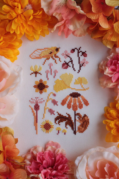 A finished cross stitch of a small, yellow, orange, and brown sampler. It features an adult yellow cicada, a cicada shell on an orange black-eyed susan flower, pink strawberries, various pink and yellow flowers, and yellow ginkgo leaves. Orange Cross Stitch, Cottagecore Cross Stitch Pattern, Yarn Hobbies, Golden Hour Nature, Embroidery Things, Flowers Cross Stitch, String Crafts, Ginkgo Leaves, Cross Stitch Collection