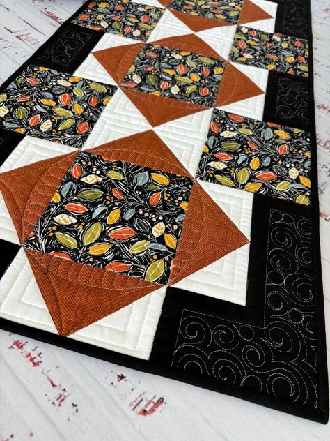 Celebrate the change of season, the cooling of temperatures, the turning of leaves with a new quilted table runner for your home.  This runner would look great on a dining table, buffet or entry table.  Lay it on the surface of your choice and enjoy it every time you catch a glimpse of it.  This runner says, "FALL". The runner is made with a multi colored leaf focal fabric, a rusty orange print, a white solid and a black solid.  The binding is the black solid fabric.  Binding was machine sewn to the front for durability, folded over and hand stitched to the back for a smooth finish.  Backing is an off-white fabric with small black plus signs. The runner is full of quilting designs.  Take a look at the photos for an up close view of the quilting. This runner has not been washed.  I recommen Dining Table Buffet, Layer Cake Quilt Patterns, Quilted Table Topper, Cake Quilt, Patchwork Table Runner, Table Buffet, Layer Cake Quilts, Quilted Table Runners Patterns, Penny Rug