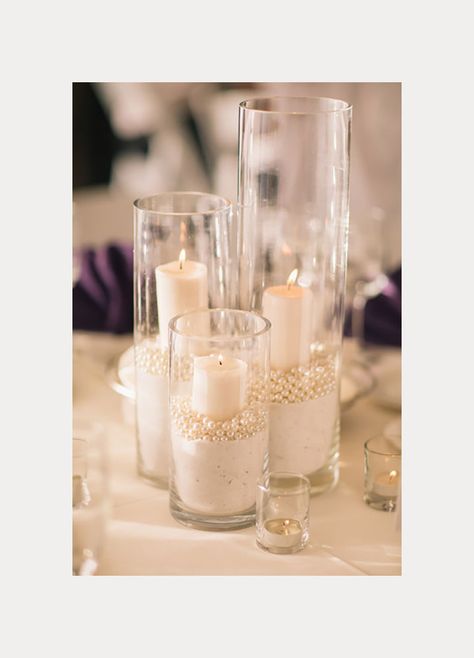 Glass cylinders filled with sand, pearls and votive candles. White Feather Centerpieces Wedding, Wedding Beads Decorations, Cylinder Glass Vase Centerpiece, Beach Centerpiece Ideas, Pearls And Bows Party, Glass Decorating Ideas, Cheap Table Decorations, Sand Candle, Centerpieces Candles