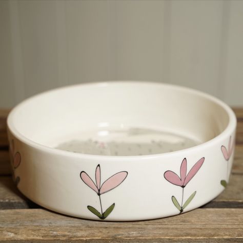 A medium-sized straight-sided dog bowl with delightful grey scruffy dog with motifs of grass and pink flowers Size W19.5cm x H5.5cm. Painted Dog Bowls Pottery, Hand Painted Dog Bowls, Clay Dog Bowl Ideas, Pottery Dog Bowl Ideas, Dog Bowl Painting Ideas, Dog Bowl Pottery Painting, Ceramic Dog Bowl Painting Ideas, Pottery Painting Dog Bowl, Painted Dog Bowl