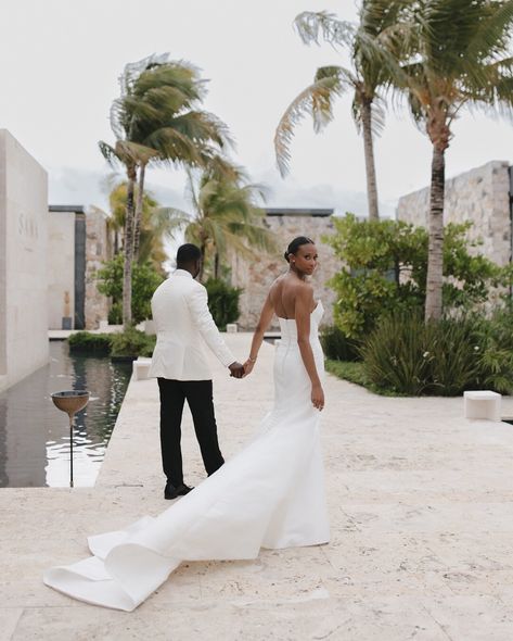 Elegant bride in fitted white gown with dramatic train holding groom's hand at tropical luxury resort with swaying palm trees and stone architecture African Beach Wedding, Trident Castle Jamaica Weddings, Travel Wedding Theme Decoration, Minimalist Wedding Design, Coastal Wedding Ideas, Destination Wedding Attire, Tropical Wedding Photography, Luxury Beach Wedding, Tropical Wedding Venue