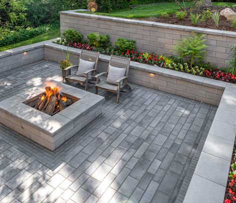 These homeowners faced a significant challenge when designing the patio of their dreams. The yard sloped into a forest backing onto their home. This was resolved by building several steps that lead to a beautiful sunken patio with a surrounding U-Cara retaining wall that showcases their lush gardens. They chose to also add a U-Cara firepit as the focal point, so their family can relax in a cozy setting.

#sunkenpatio #retainingwall #gardenwall #patio #firepit #beautifulbackyard Patio Wall Ideas, Evening Picnic, Retaining Wall Patio, Backyard Retaining Walls, Sunken Patio, Sloped Backyard, Landscaping Retaining Walls, Sloped Garden, Patio Wall