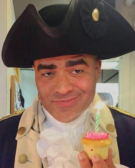 Christopher Jackson dressed as General George Washington (complete with tricorn hat) is smirking while holding in his left hand, a very tiny vanilla cupcake with pink frosting and a small green candle which is lit, the light of which is reflected in the actor’s dark brown eyes. George Washington Hamilton, Washington Hamilton, Hamilton George Washington, Cast Of Hamilton, Christopher Jackson, Hamilton Cast, Musicals Funny, Hamilton Jokes, Hamilton Fanart