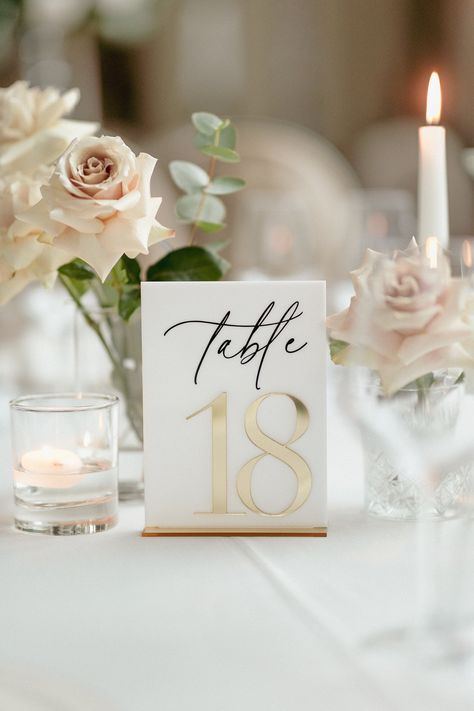 "Elevate Your Table Setting: Add a touch of elegance and sophistication to your wedding tables with our White Acrylic Table Numbers with Gold Mirror Stands. These exquisite signs are designed to enhance your wedding decor, perfectly balancing functionality and style. Chic White Acrylic Numbers: Each table number is beautifully crafted from high-quality white acrylic, ensuring visibility and elegance. The crisp, clean white design offers a modern yet timeless look, ideal for any wedding theme. Luxurious Gold Mirror Stands: Complementing the white acrylic numbers, the gold mirror stands provide a stable and stylish base, adding a touch of glamour and ensuring each number stands out on your tables. Versatile and Timeless Design: Our table numbers are designed to complement any wedding decor, Champagne Table Numbers, Table Designs Wedding, White And Black Table Numbers, Beige And Gold Wedding Theme, Simple Elegant Wedding Decor, Gold And White Wedding Decorations, White And Gold Table Decor, White And Gold Wedding Table, Modern Minimalist Wedding Decor