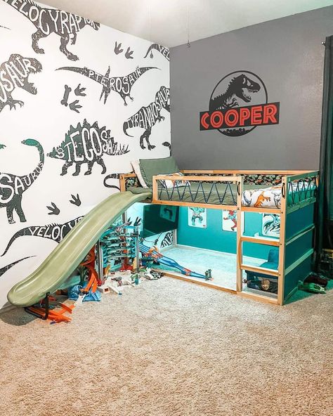 Surprise your son with a fun Jurassic World-themed bedroom. The adorable tiny bunk bed with olive sheets features a slide attached to its side. Complete the space with two dinosaur-themed accent walls. Dinosaur Room Ideas Toddler, Kids Dinosaur Bed, Small Dinosaur Bedroom Ideas, Dino Inspired Bedroom, Toddler Boy Room Decor Dinosaur, Dinosaur Boy Room Ideas, Jurassic World Room Decor, Little Boys Dinosaur Bedroom, Big Boy Dinosaur Bedroom