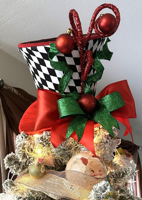 This Christmas tree top topper hat and/or centerpiece is sold, but no worries, we can make one just for you.   This is a festive, whimsical handcrafted Christmas tree topper top hat and or centerpiece. It features a top hat with a black and white checkered pattern.  It is adorned with red and green embellishments, such as ribbons, ornaments, and decorative spirals, making it ideal for holiday decor or a whimsical centerpiece.  Use it to decorate anywhere in your home as a decorative centerpiece and place it at any focal point to enhance your decor.     The measurements are 11.5 inches tall from the highest point of the red spirals x 12  inches at the brim. The top hat is uniquely made with a cavity opening on the top and bottom. The bottom is used to insert the tree branch and secure the h Hat Tree Toppers Christmas, Whimsical Tree Topper, Top Hat Christmas Tree Topper, Top Hat Christmas Tree, Hat Christmas Tree Topper, Christmas Top Hat, Top Hat Centerpieces, Top Hat Tree Topper, Whimsical Centerpiece