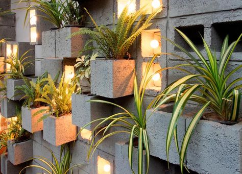 Concrete blocks were used to create this modern eye-catching accent wall, with some of them turned to become planters, slightly protruding to make room for the plants. Other blocks have been turned on their side to make room for individual light bulbs adding a soft glow of the light to the scene. #ConcreteBlockPlantWall #ConcreteBlockPlanter #CinderBlockPlanter Playground Restaurant, Cinderblock Planter, Compound Wall Design, Concrete Block Walls, Planter Wall, Cinder Blocks, Compound Wall, Concrete Block, Planter Design