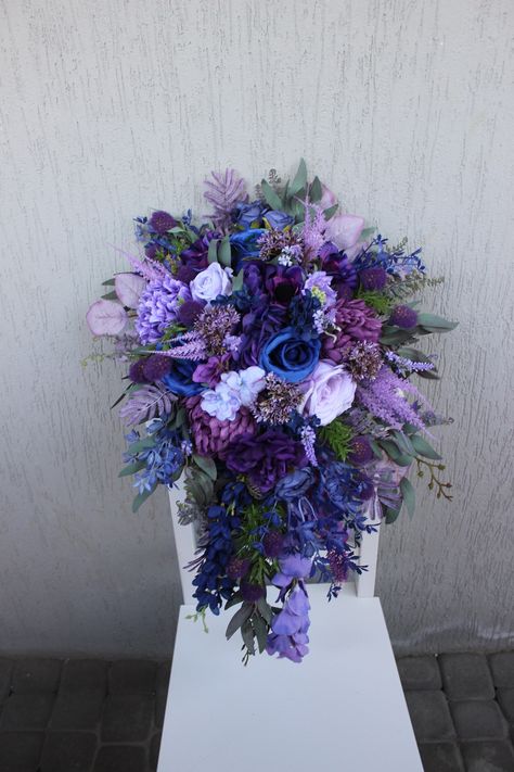 Immerse yourself in the enchanting beauty of our exquisite bouquet featuring jewel-toned hues. This cascading bridal bouquet, adorned in a blend of navy, purple silk flowers, roses, and eucalyptus, radiates elegance and sophistication, reflecting the unique beauty of your special day. From the bold tones of teal to the depths of purple, this artificial bouquet creates a refined arrangement that not only adds charm to your wedding ensemble but also serves as an unforgettable symbol of your love and unity. ○ Color: jewel tone, blue, navy, purple, lavender, green ○ Personalization: I can make changes to your wishes ○ Processing time: 1 - 2 weeks ○ Shipping time: 14 - 25 business days NOTE ○ I ship with REGISTERED mail and you will get a tracking number. ○ All items will be carefully packed in Purple Blue Centerpiece, Navy Purple And Green Wedding, Dark And Light Purple Wedding, Blue Purple Bouquet Wedding, Dark Blue Purple Wedding, Dark Blue And Dark Purple Wedding, Bridal Bouquet Fall Blue, Light Purple And Navy Blue Wedding, Royal Purple And Navy Blue Wedding