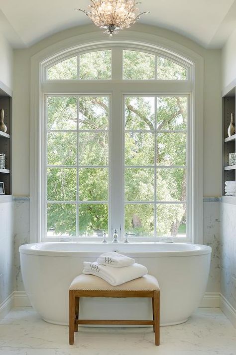 Freestanding oval tub under arched windows in a transitional master bathroom boasting a bathtub bench atop marble floor tiles. Bath Under Window, Bathtub Bench, Oval Tub, Arch Windows, Marble Floor Tiles, Oval Bathtub, Bath Window, Luxury Master Bathrooms, Bloxburg Modern