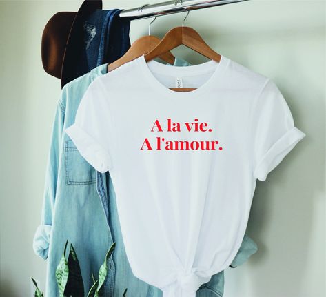 "This funny french shirt displays a la vie, a l'amour. This funny classic softstyle definition tshirt, makes a perfect french gift for him or her to celebrate love with a french twist. 'To love, To life' in French Welcome to our Etsy shop 🧡  FREE Shipping Please see the picture for Sizing (the sizes are UNISEX) & Shipping information below. 👇🏼 This classic unisex jersey short sleeve tee fits like a well-loved favorite. Soft cotton and quality print make users fall in love with it over and ove Definition Tshirt, Shirt Displays, Minimal Shirt Design, French Gifts, Funny French, Shirt Display, French Twist, Bella Canvas Tees, Funny T Shirt