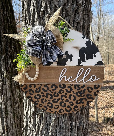 Welcome guests with this beautiful cow print with leopard door hanger.  Entire hanger is laser cut, painted and sealed.  3D layered sign, NO STICKERS OR VINYL HERE!  ABOUT THIS DOOR HANGER: ⚬ Greenery/Bow are included and secured with staples ⚬ Laser cut rounds from maple wood (not MDF), more dense and sturdy than birch. ⚬ Comes with ribbon/rope attached to hang sign ⚬ Has a string of beads and tassel attached  ⚬ Back is unfinished ⚬ Wood is sealed so that it is suitable for outdoor use (please see recommended locations for signs below) ABOUT SHIPPING: ⚬ Please see "estimated shipment date" prior to purchasing ⚬ Handmade in the order in which received ⚬ "In stock quantity" is so that multiple people can purchase at one time ⚬ Cancellations are not accepted ⚬ Mailed priority mail; mail dela Cow Print Wreath, Leopard Door Hanger, Western Door, Farmhouse Door Hanger, Welcome Signs Front Door, Welcome Door Hanger, Home Wooden Signs, Farmhouse Door, Hanger Crafts